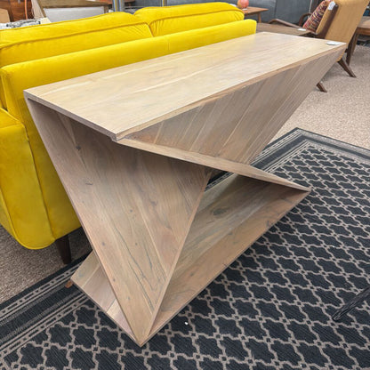 Wooden table with a geometric design in a room with yellow couches and patterned rug.