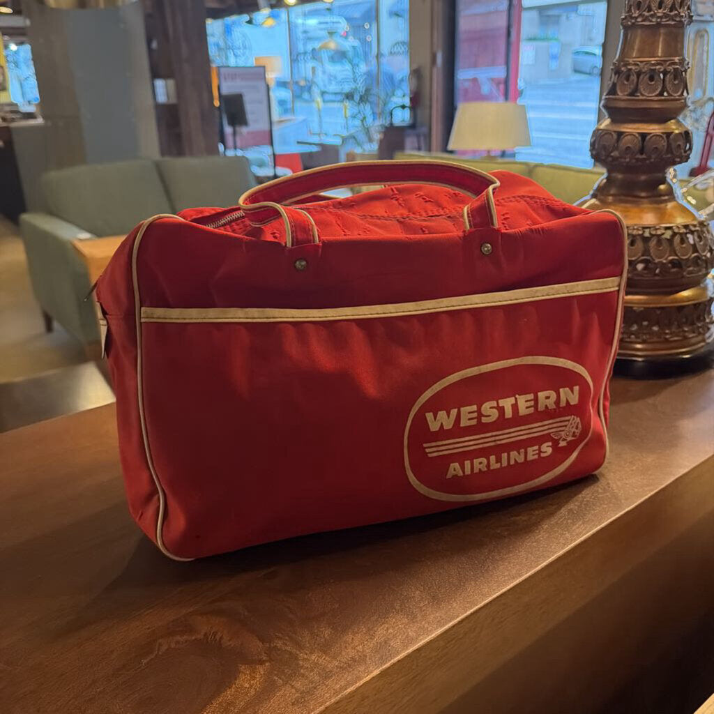 This authentic vintage flight bag is a nostalgic piece of aviation history from the legendary Western Airlines. The bag is constructed from a durable vibrant red canvas or vinyl and features the iconic white "Western Airlines" logo prominently displayed within an oval on the front.