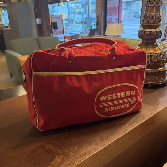 This authentic vintage flight bag is a nostalgic piece of aviation history from the legendary Western Airlines. The bag is constructed from a durable vibrant red canvas or vinyl and features the iconic white "Western Airlines" logo prominently displayed within an oval on the front.