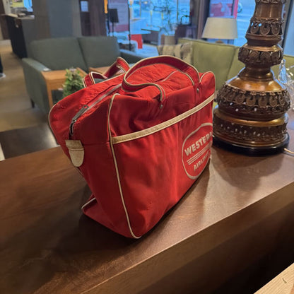 This authentic vintage flight bag is a nostalgic piece of aviation history from the legendary Western Airlines. The bag is constructed from a durable vibrant red canvas or vinyl and features the iconic white "Western Airlines" logo prominently displayed within an oval on the front.
