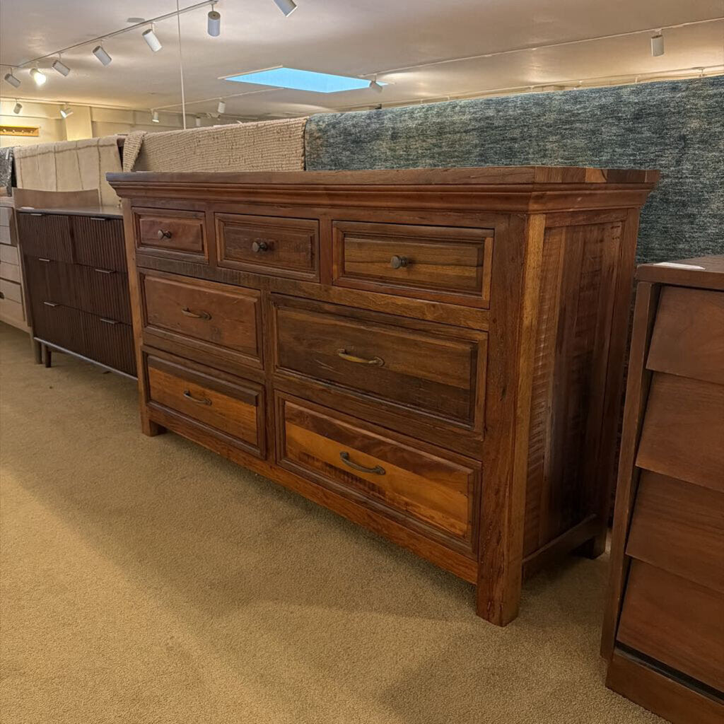 Wooden dresser in a showroom setting with other furniture pieces.