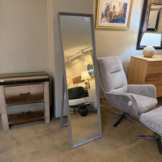 Room interior with a large floor mirror, gray armchair, and wooden furniture.