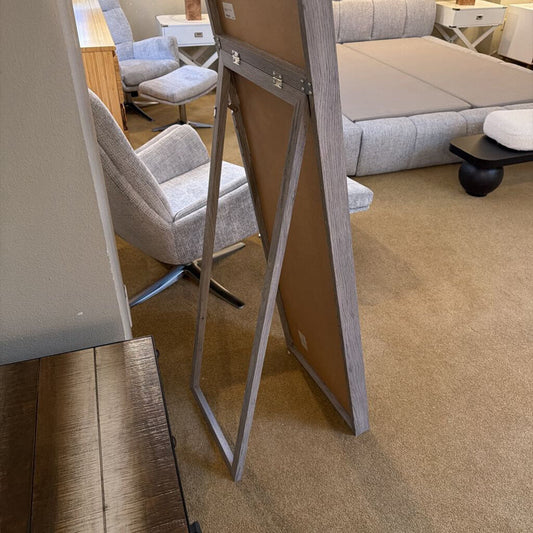 Easel stand with a wooden board in an indoor setting, possibly a furniture store.