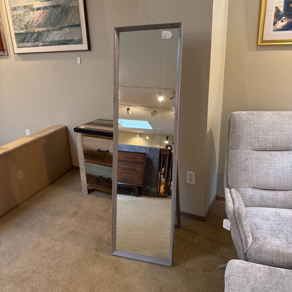 Full-length mirror leaning against a wall in a room with furniture and decor.