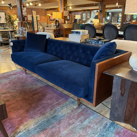 Blue tufted sofa in a room with wooden floors and colorful rug