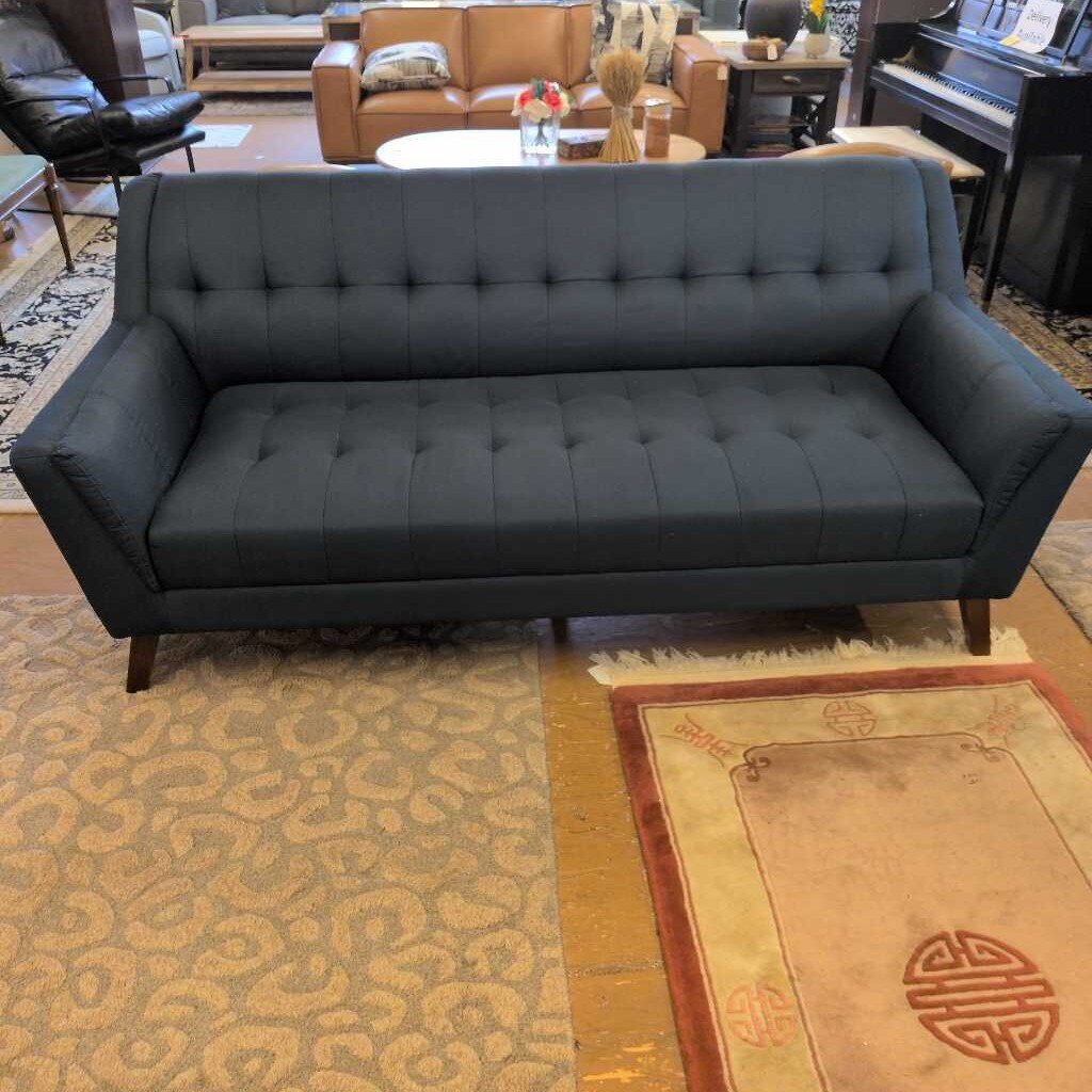Gray tufted sofa in a room with patterned rugs and furniture.