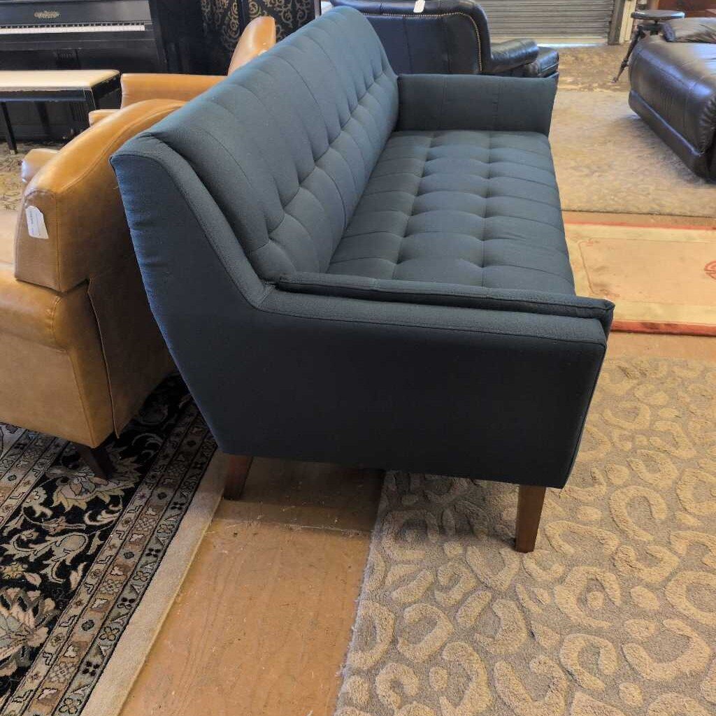 Gray tufted sofa in a showroom setting with other furniture.