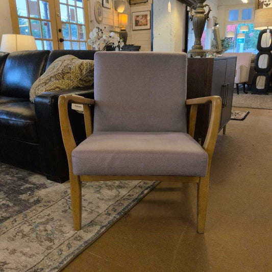 Gray upholstered chair in a room with a black leather couch and decorative items.