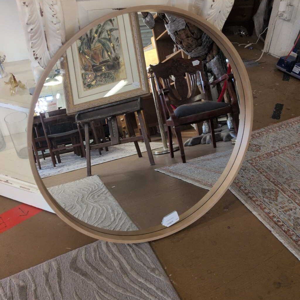 Round mirror with wooden frame reflecting a room with furniture and decor.