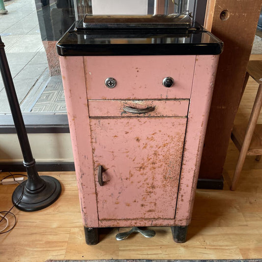 Rustic pink metal cabinet with a black top on a wooden floor.