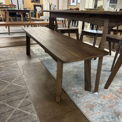 Wooden dining bench in a showroom setting with tables and chairs.