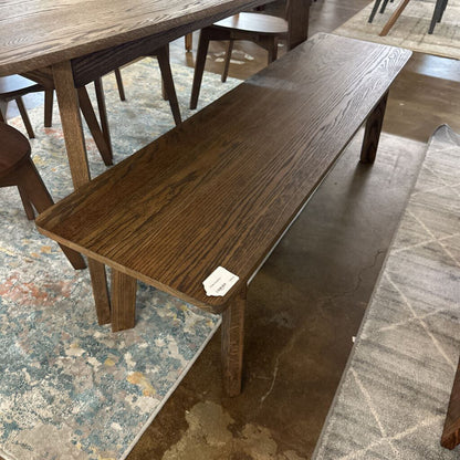 Wooden bench in a room with a table and chairs on a patterned floor.