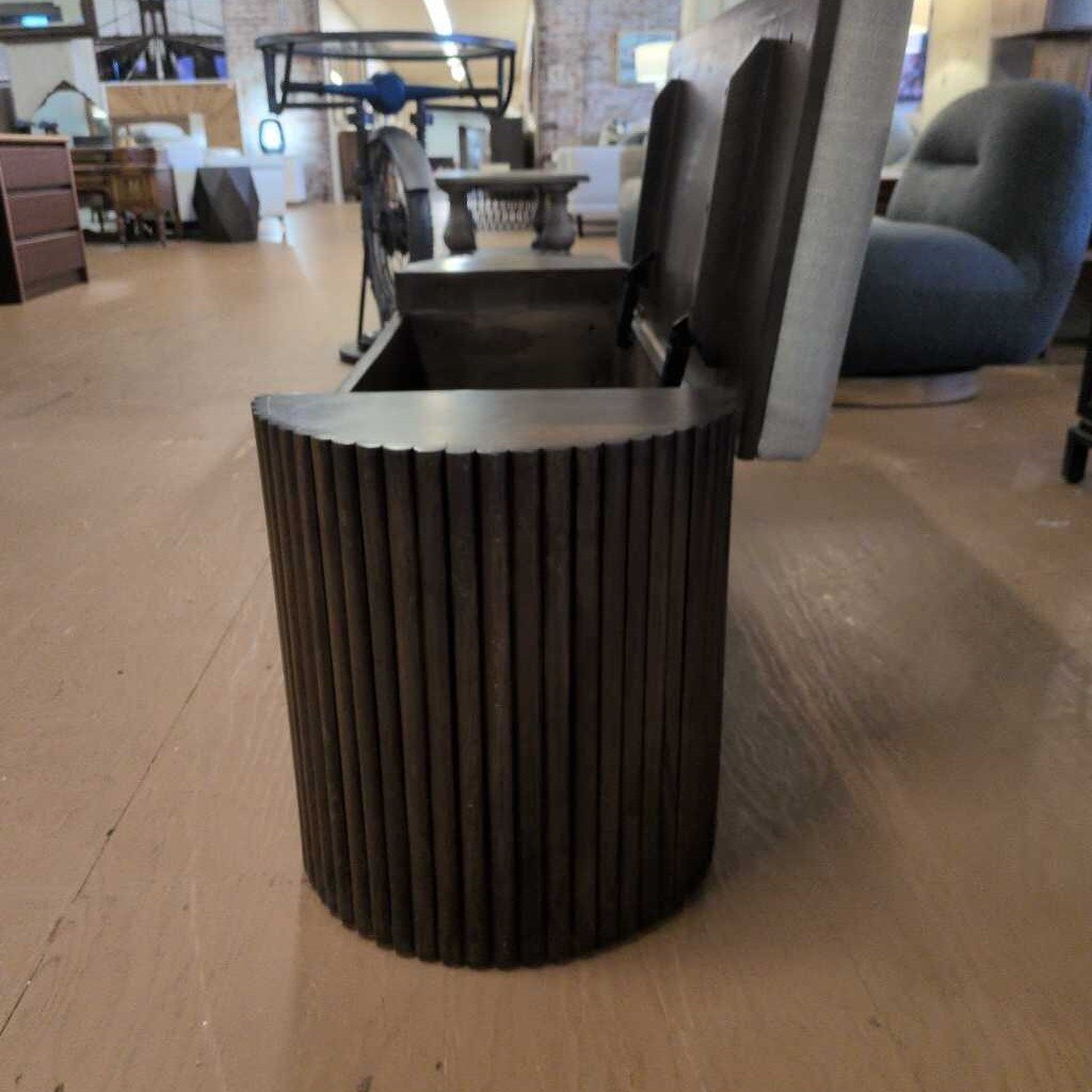 Dark cylindrical trash can on a wooden floor with blurred background