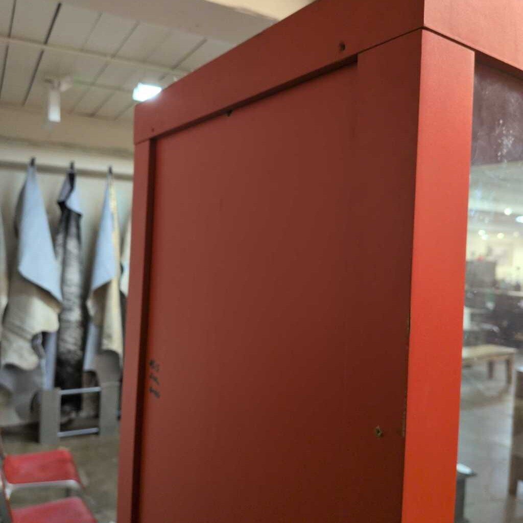 Red cabinet with a blurred background of a room with clothes and chairs.
