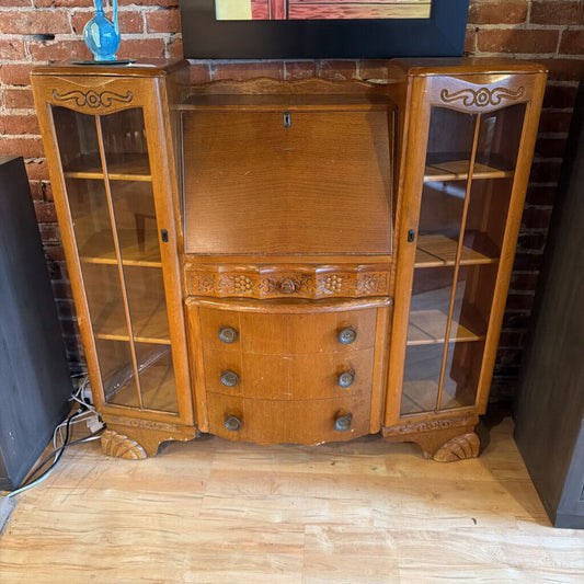 Wooden cabinet with glass doors against a brick wall.
