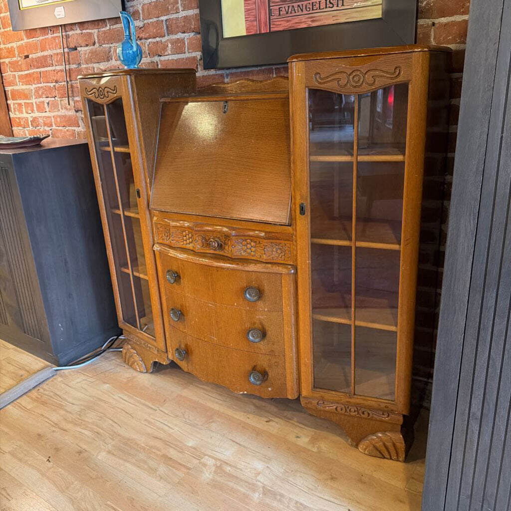 Wooden secretary desk with glass panels against a brick wall.