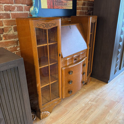 Wooden cabinet with glass doors and drawers against a brick wall.