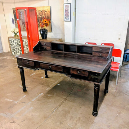 Large wooden desk in a room with red chairs and a white wall.