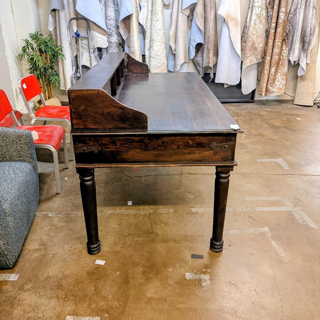 Dark wooden desk in a room with red chairs and hanging clothes