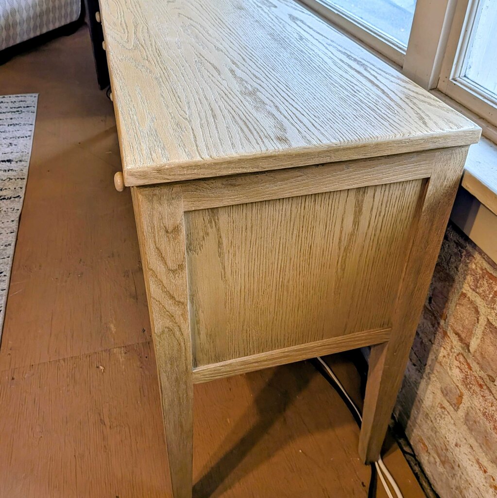 Wooden side table with a textured surface in a room with a wooden floor and brick wall.