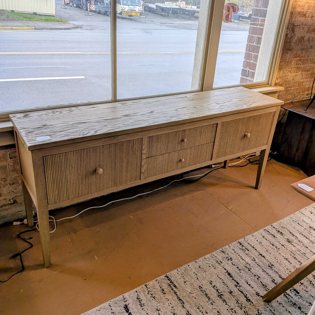 Wooden console table in a room with large windows showing an outside view.