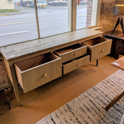 Wooden dresser with multiple drawers in a room with a window view of a street.