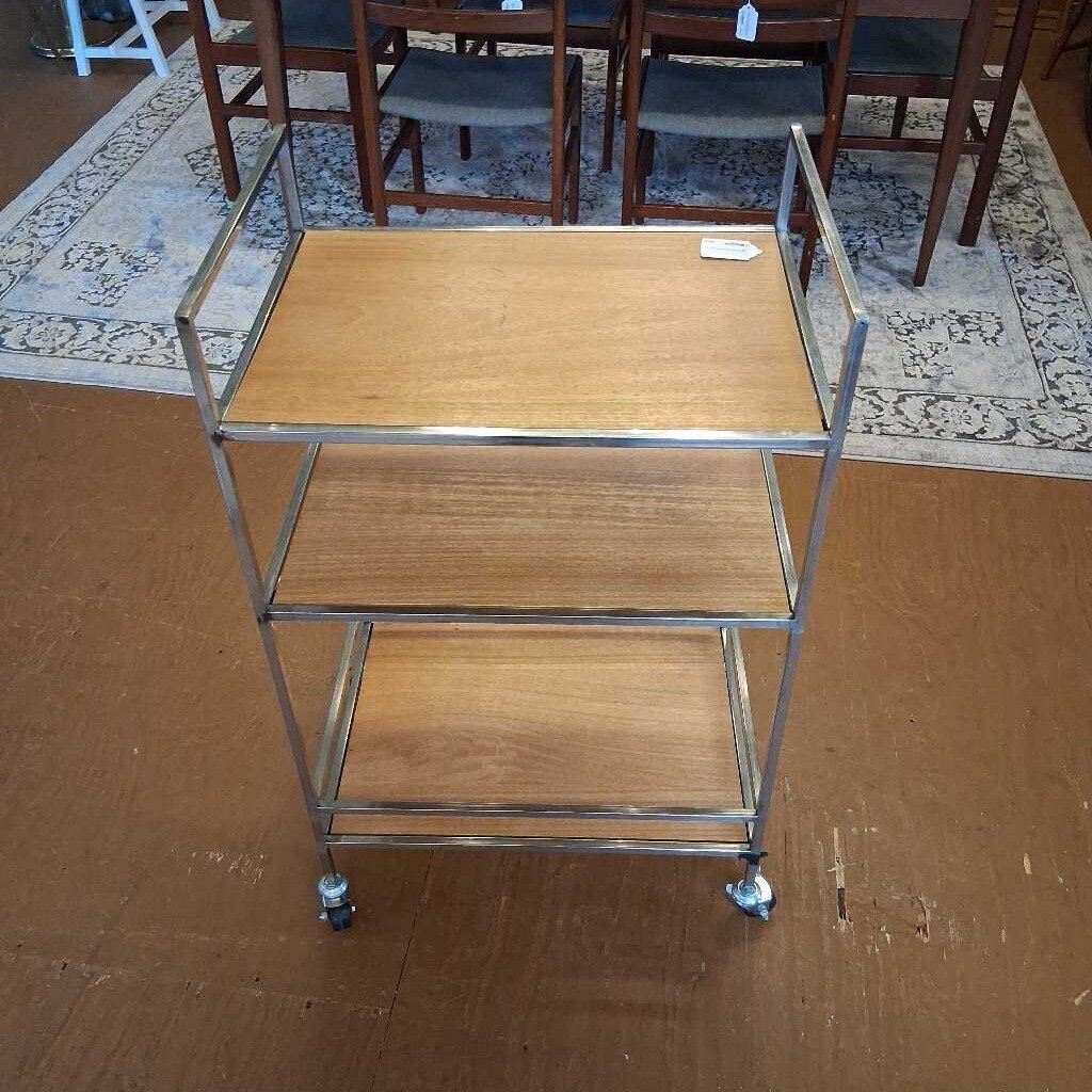 Three-tier metal serving cart with wooden shelves on a wooden floor.