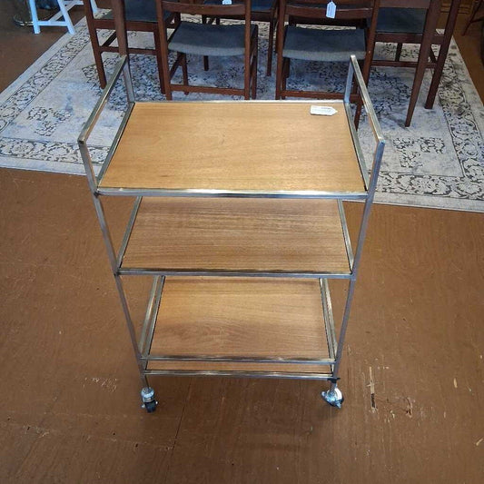 Three-tier metal serving cart with wooden shelves on a wooden floor.