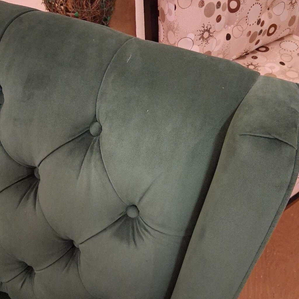 Green tufted cushion on a sofa with a patterned fabric background