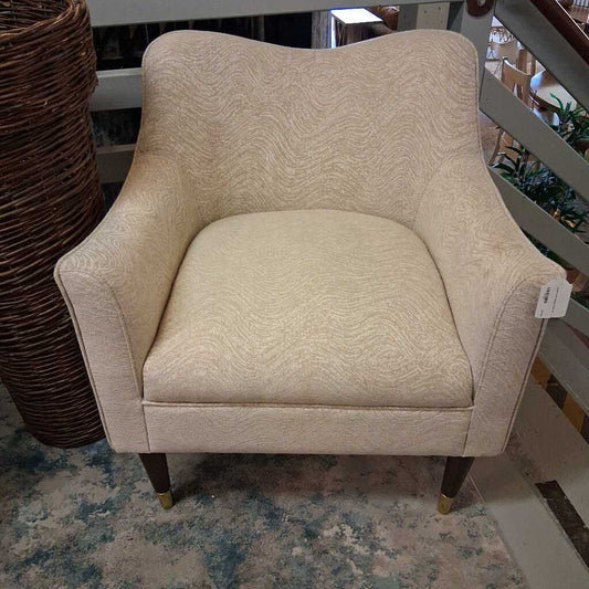 Beige armchair with a textured pattern on a floor with a wicker basket in the background.