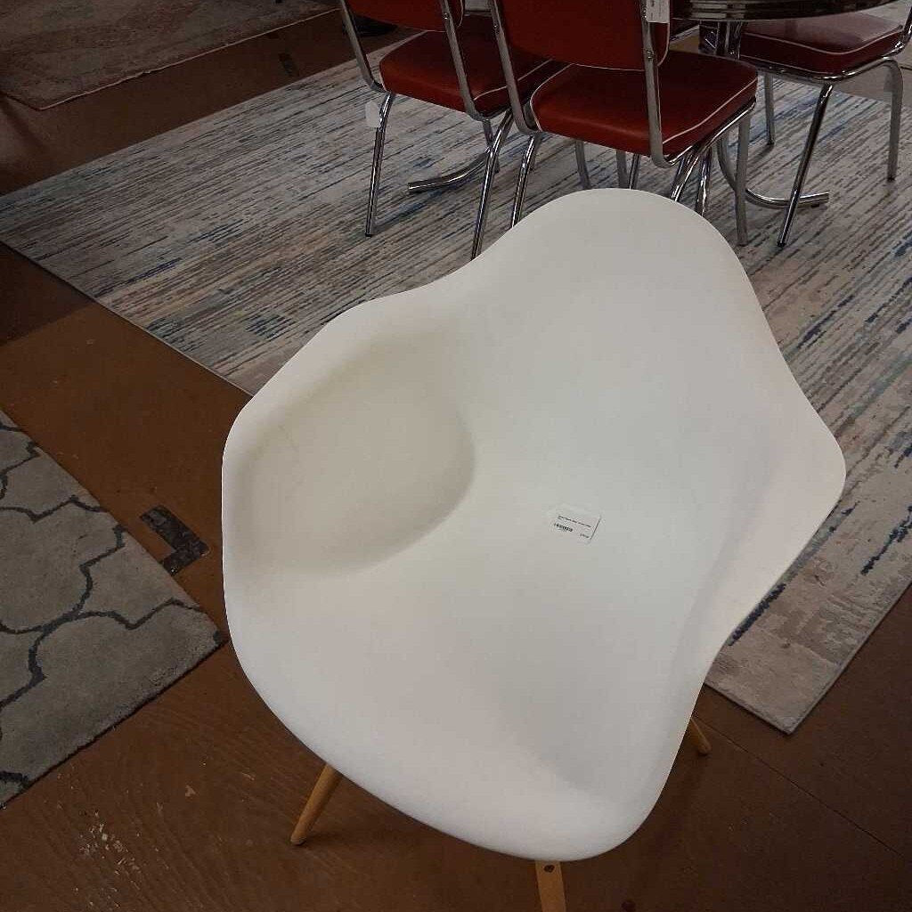 White chair with wooden legs on a wooden floor, with other chairs and a rug in the background.