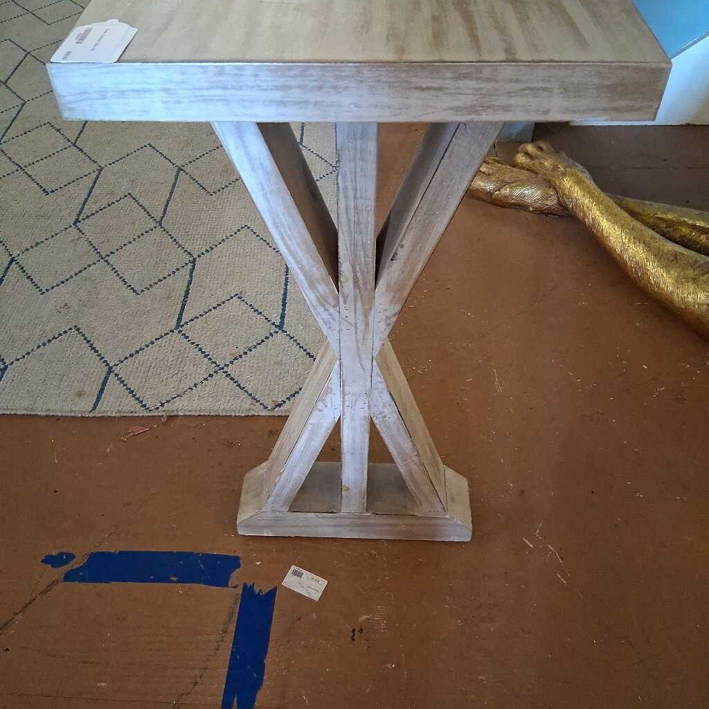 Wooden table with a unique base design on a brown floor.