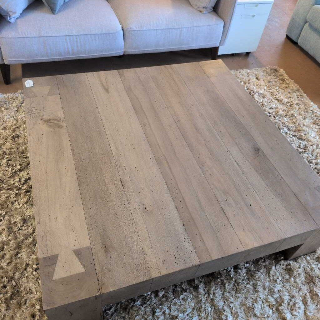 Wooden coffee table in a living room setting with a sofa and rug.