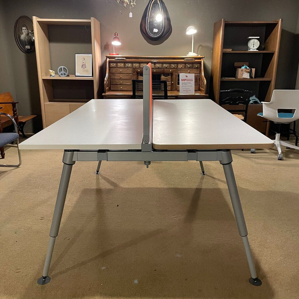 The desk comprises two off-white laminate work surfaces with a thin, natural wood-effect edge. Dividing the two stations is a vibrant orange fabric privacy screen that serves as a visual barrier and an acoustic damper. 