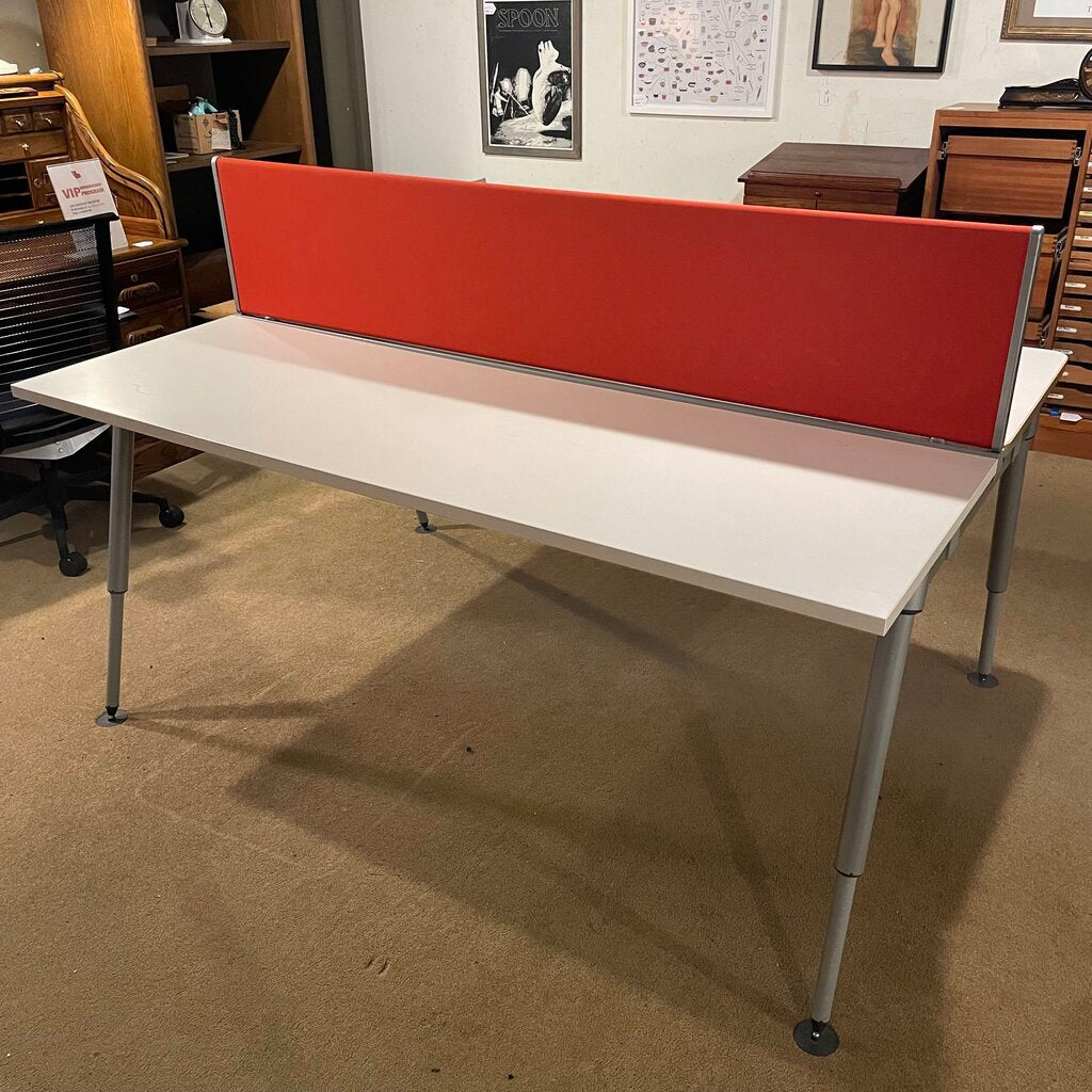 The desk comprises two off-white laminate work surfaces with a thin, natural wood-effect edge. Dividing the two stations is a vibrant orange fabric privacy screen that serves as a visual barrier and an acoustic damper. 