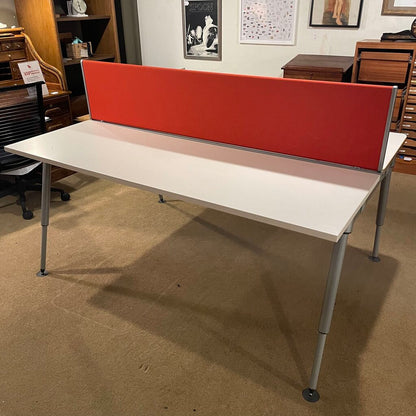 The desk comprises two off-white laminate work surfaces with a thin, natural wood-effect edge. Dividing the two stations is a vibrant orange fabric privacy screen that serves as a visual barrier and an acoustic damper. 
