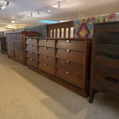 Row of wooden dressers in a store setting with a colorful rug on the wall.