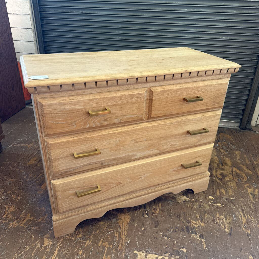 Wooden dresser with brass handles on a concrete floor.
