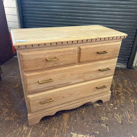 Wooden dresser with brass handles on a concrete floor.