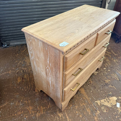 Wooden chest of drawers with brass handles on a rough floor.