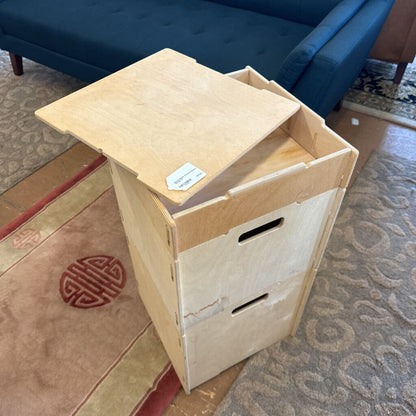 Wooden box with a lid on a patterned floor, with a blue couch in the background.