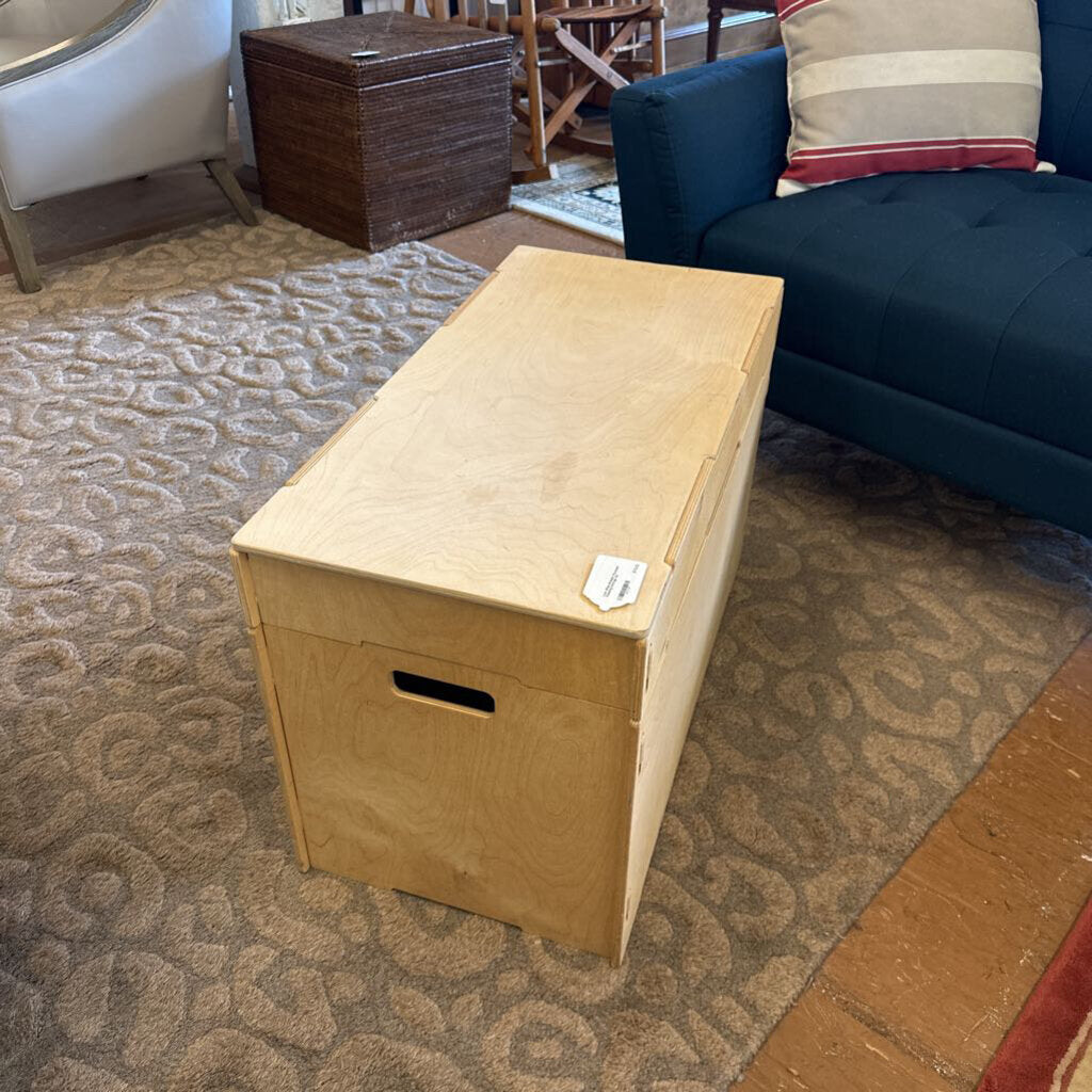 Wooden storage bench on a patterned rug with a couch in the background