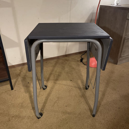 Black folding table with gray metal legs on a carpeted floor.