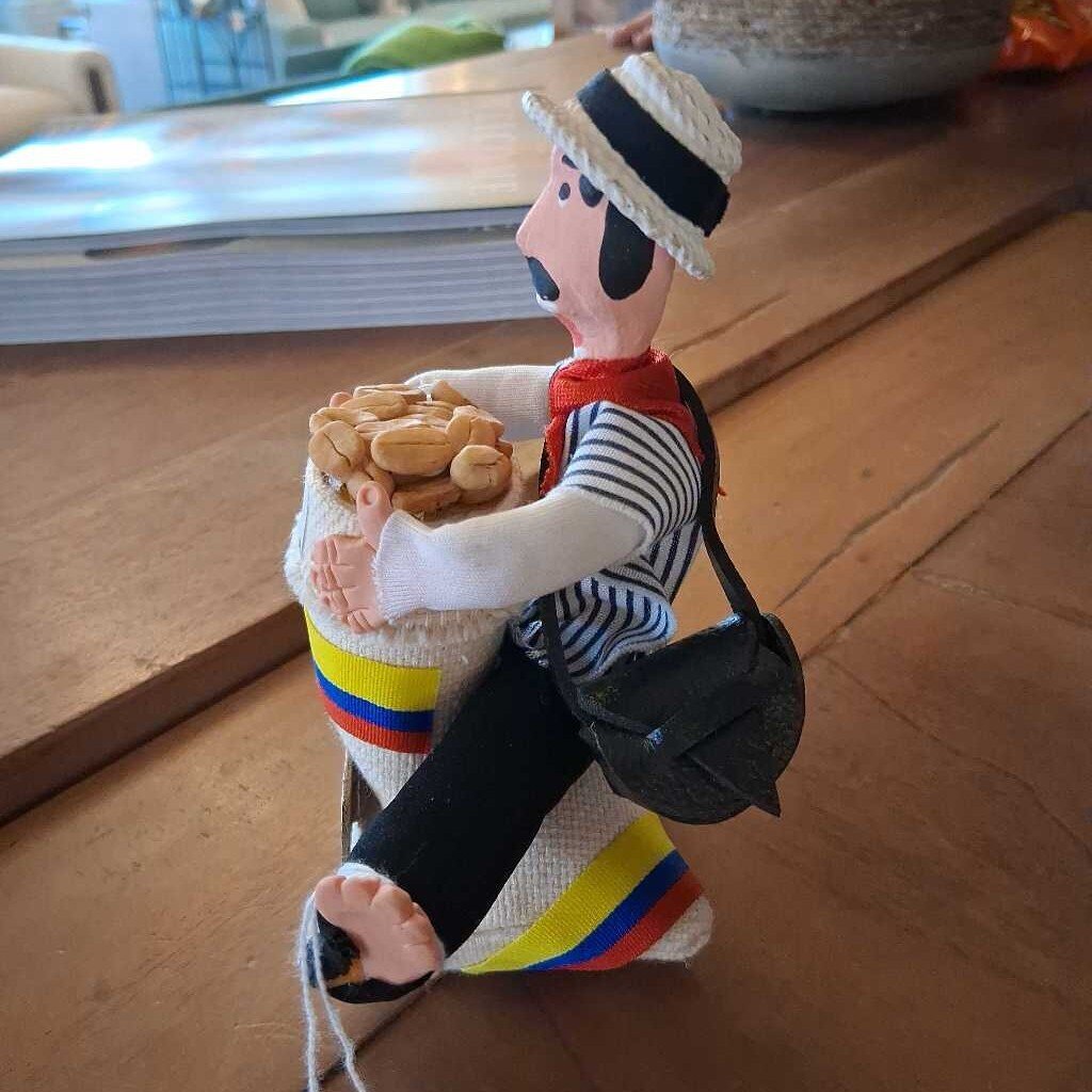 Toy figure of a person in a colorful outfit holding a bag of bread on a wooden surface.