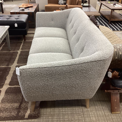 Gray textured sofa in a showroom setting with other furniture.