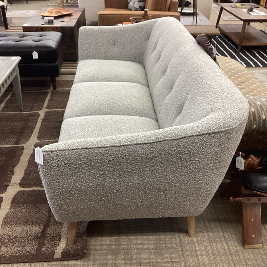 Gray textured sofa in a showroom setting with other furniture.