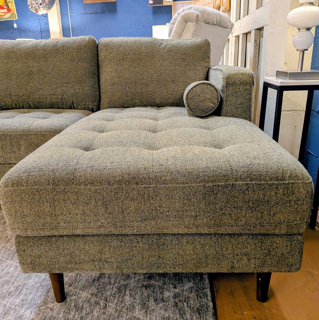 Green textured sectional sofa in a room with a blue wall and wooden floor.