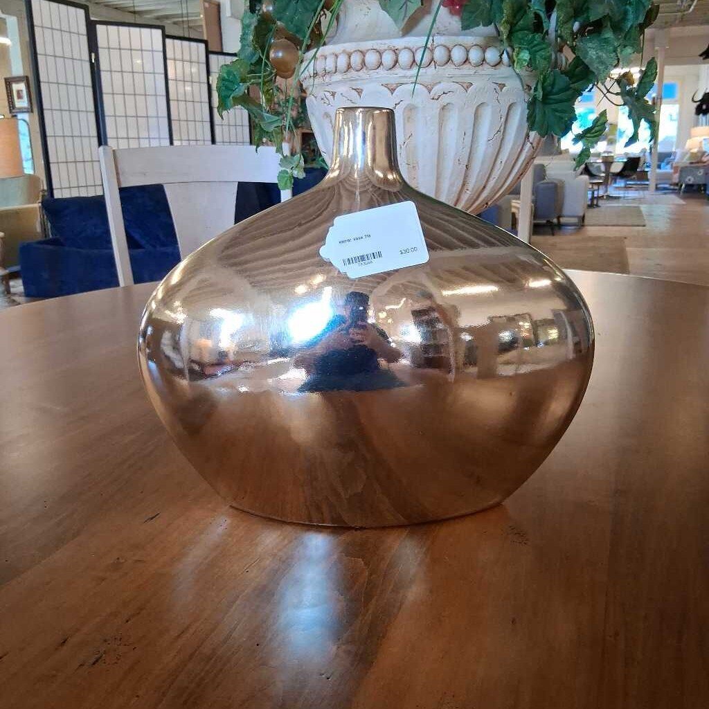 Gold decorative vase on a wooden table with a blurred indoor setting in the background