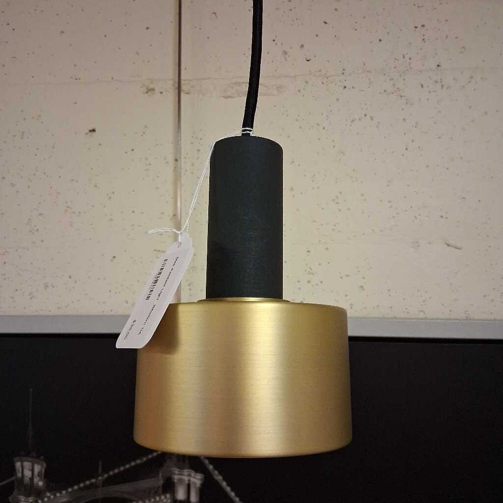 Gold pendant light with black bulb holder against a neutral wall.