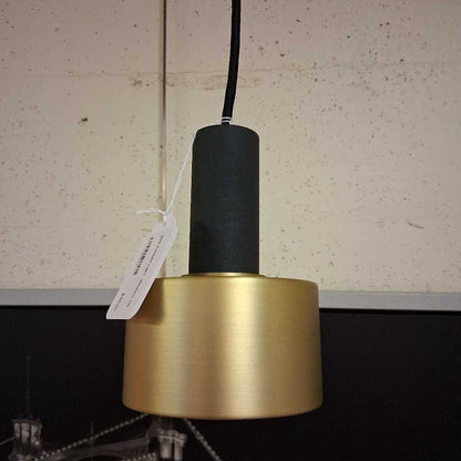 Gold pendant light with black bulb holder against a neutral wall.